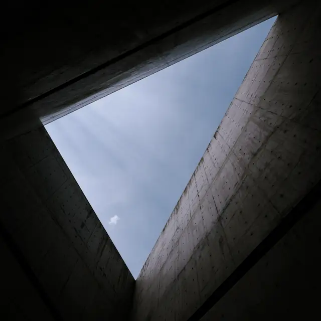 Abertura triangular num teto de concreto aparente, com o céu azul ao fundo.